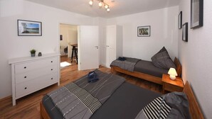 Ett sovrum med två sängar, en byrå, ett skrivbord och en dörr som leder till ett annat rum.