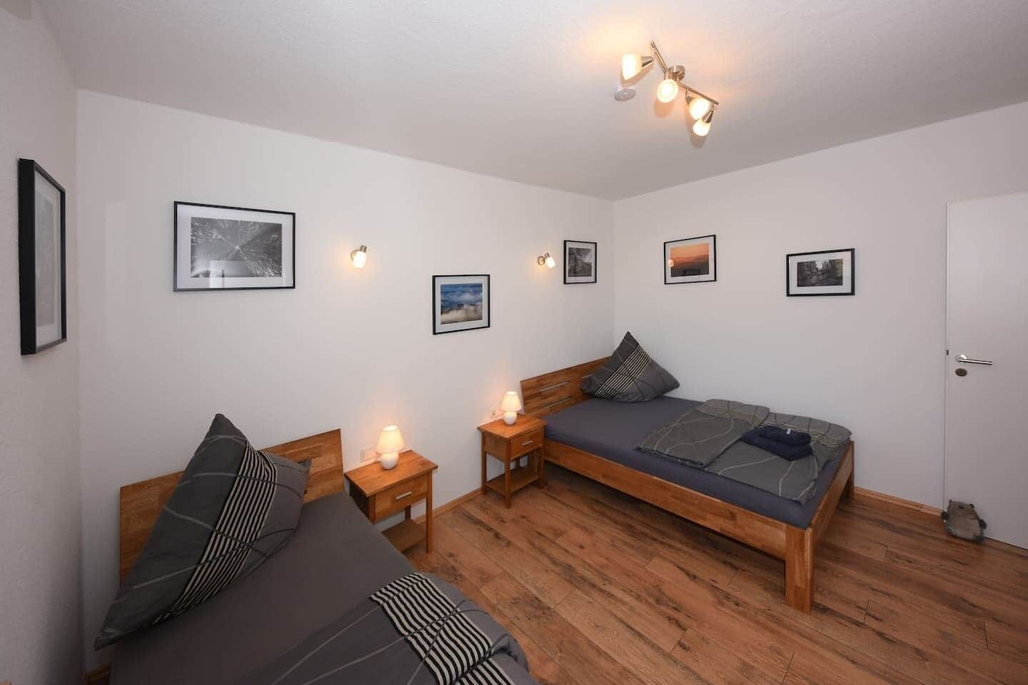 A bedroom with two beds, wooden flooring, and wall-mounted lights.