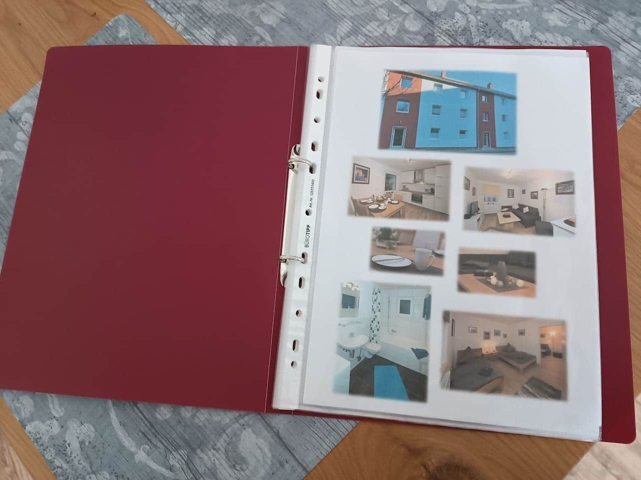 A red binder with a page displaying a blue building and interior photos of a kitchen, dining area, and living room.
