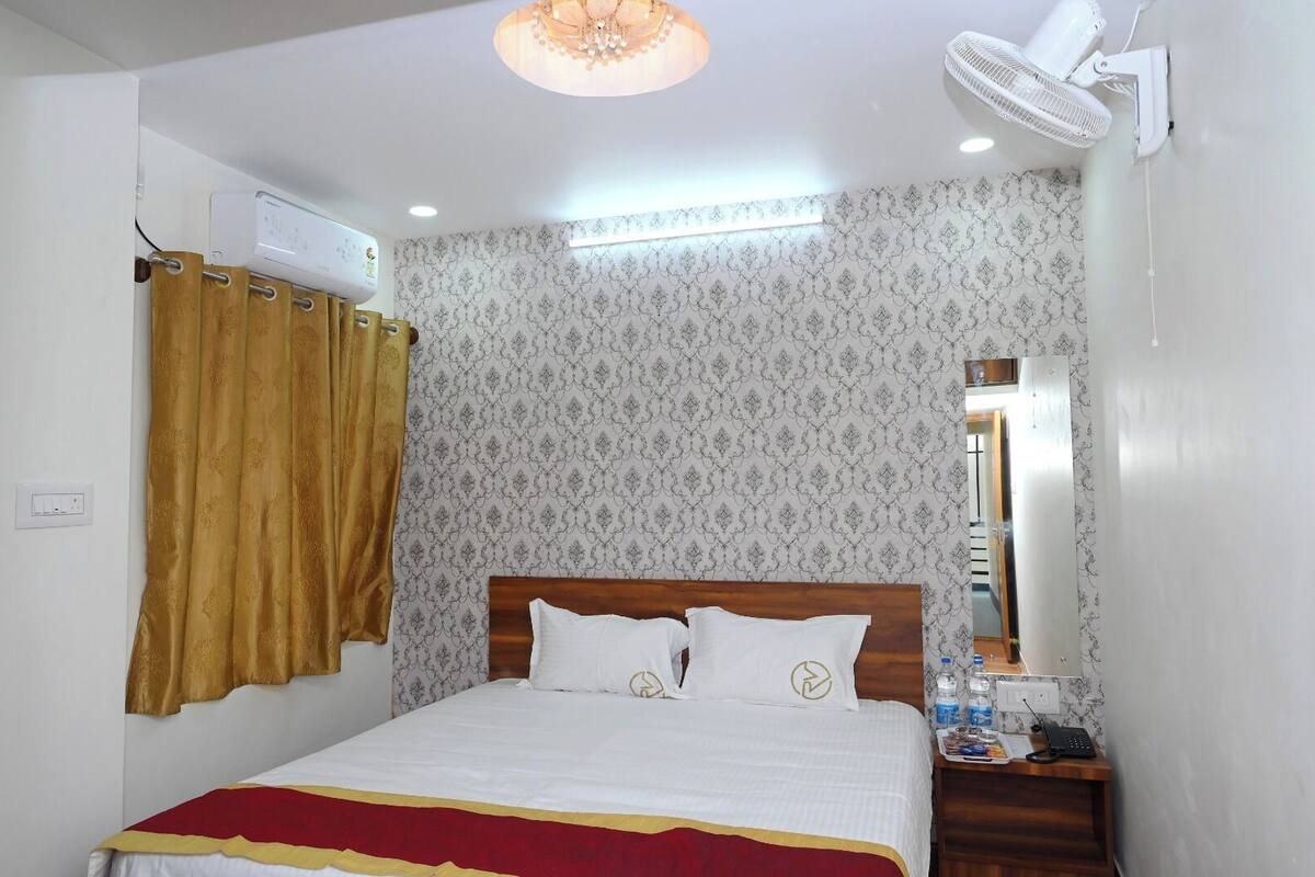 Een slaapkamer met een bed, een nachtkastje met een lamp, een spiegel en een airconditioning.