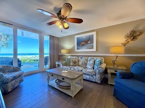 A living room with a ceiling fan, a sofa, a coffee table, and a view of the ocean. - Pelican Walk 109 - Beachfront Bliss and Poolside! (Panama City Beach)