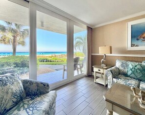 A room with a large sliding glass door leading to a beach view, a sofa, a small table, and a lamp. - Pelican Walk 109 - Beachfront Bliss and Poolside! (Panama City Beach)