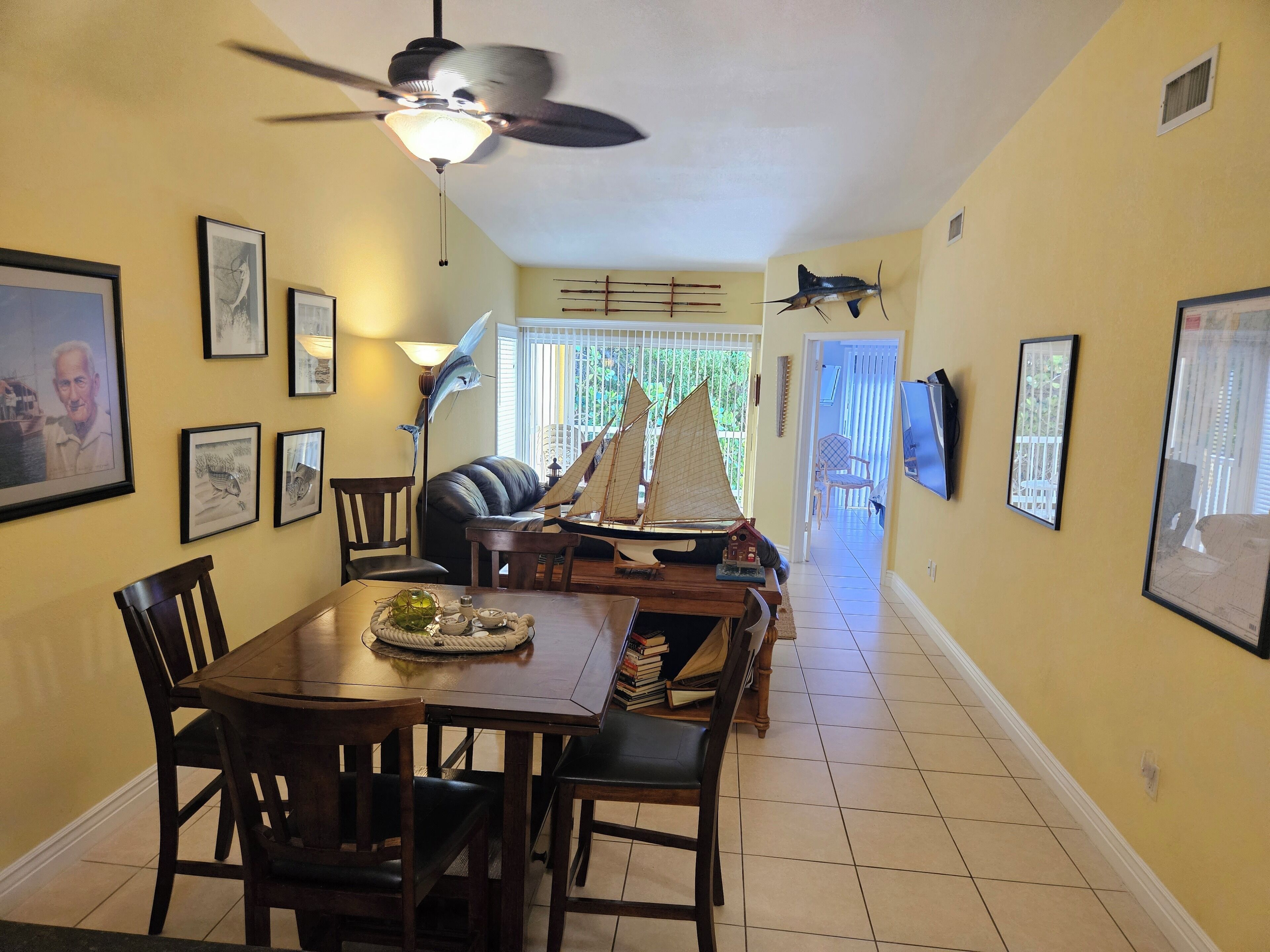 A dining area with a table, chairs, a ceiling fan, and framed artwork on the walls.