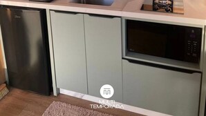 A compact kitchen with a sink, stove, and dishwasher, featuring a window with blinds and a countertop with various utensils. - Via Kairos - Rancho Queimado - SC (Rancho Queimado)
