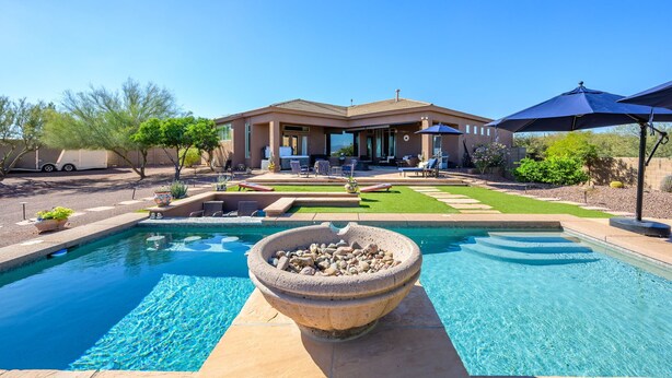 A swimming pool with a stone basin in the foreground, a patio area with outdoor furniture, and a house in the background. - A Desert Oasis w/ 4 Peaks Mountain Views! (Scottsdale)