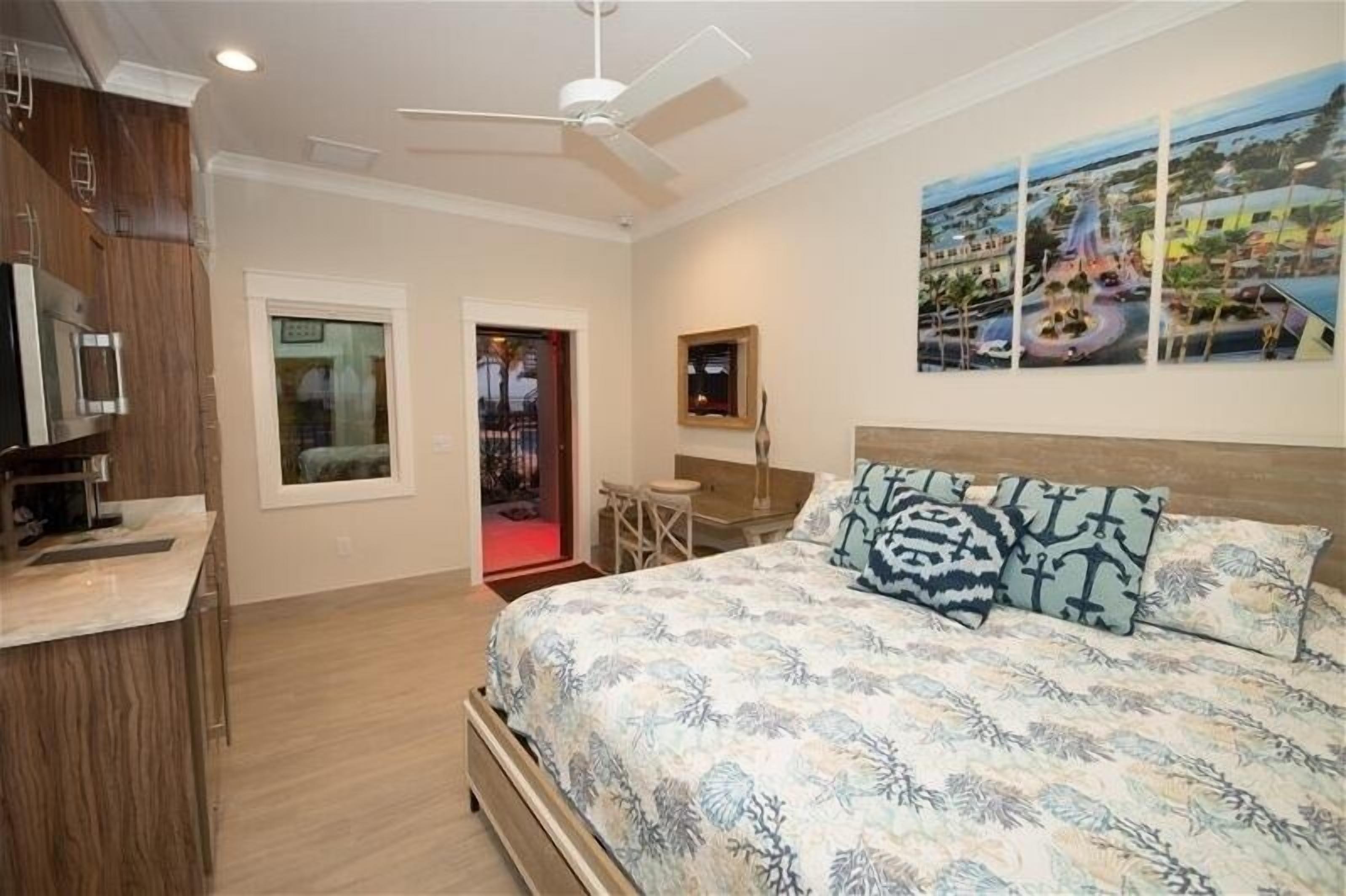 A bedroom with a bed, a desk, a chair, a TV, and a ceiling fan.