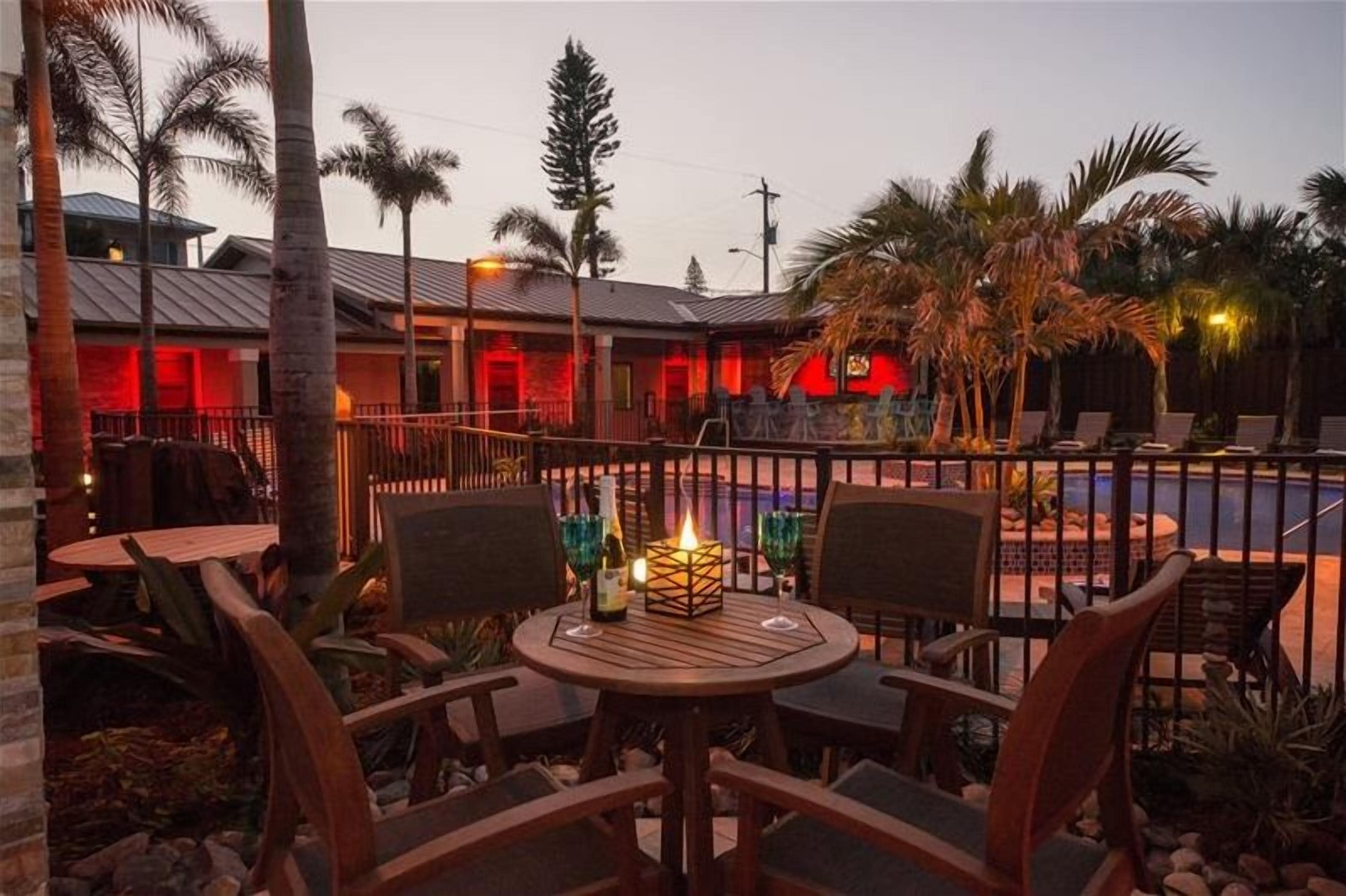Un espace patio avec des tables et des chaises rondes, une piscine et un bâtiment illuminé en rouge en arrière-plan.