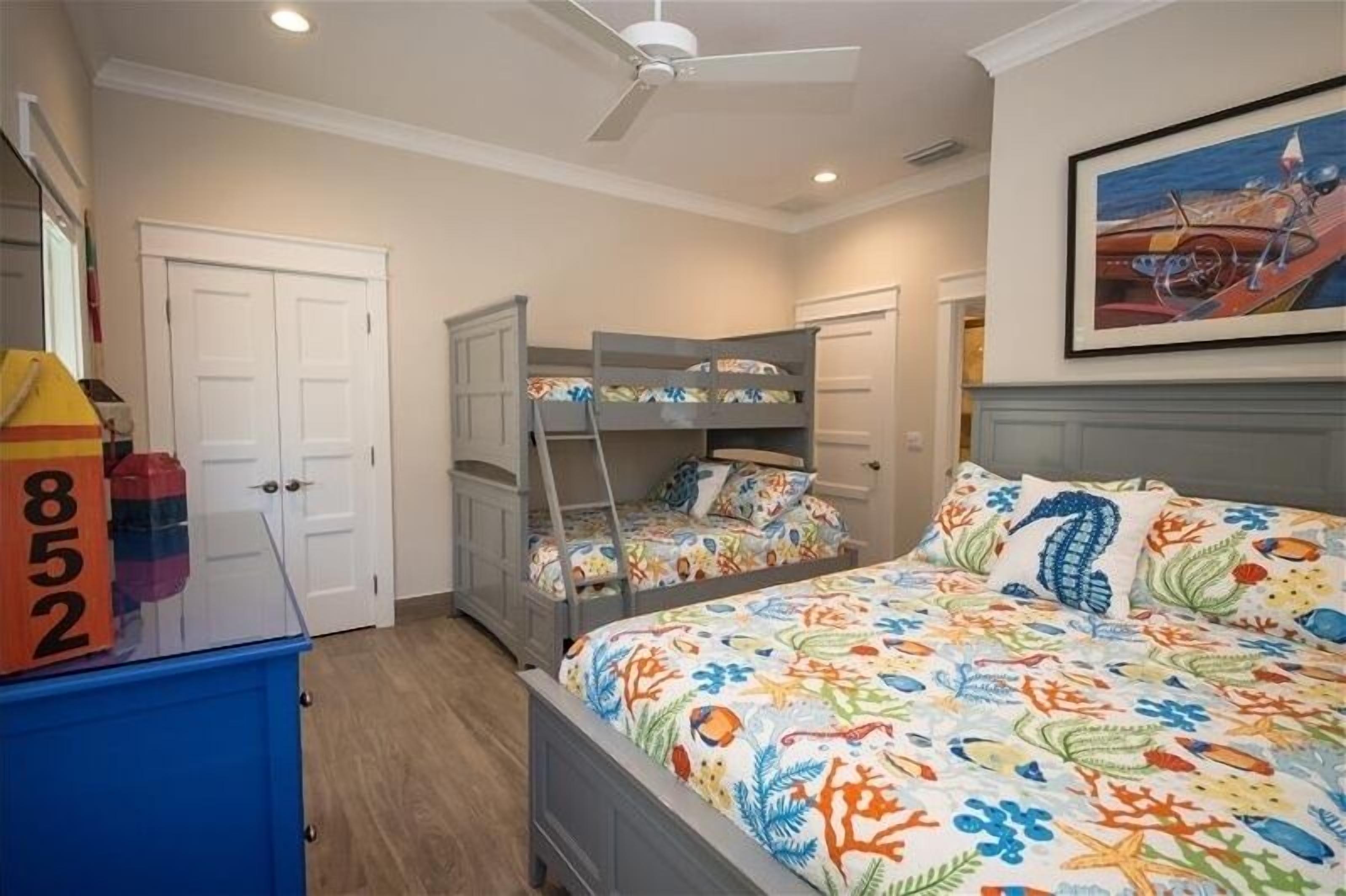 A bedroom with bunk beds, a ceiling fan, a bed with a colorful floral bedspread, and a painting on the wall.