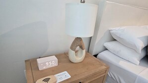 A wooden bedside table with a lamp, a digital clock, a welcome sign, and a wireless charging pad. - Barefoot Cottage A Quiet Coastal Retreat (annapolis)