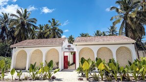 Un edificio bianco con una porta rossa e finestre ad arco, circondato da palme e piante tropicali.