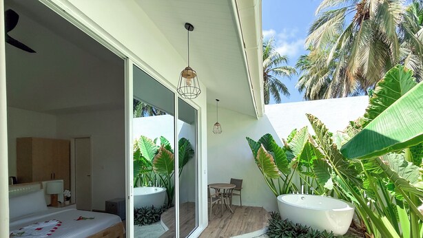Una camera da letto moderna con un letto grande, un tavolino e una finestra che si affaccia su un giardino con piante tropicali.