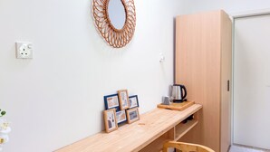 Una stanza minimalista con una scrivania in legno, uno specchio, un armadio e un bollitore.
