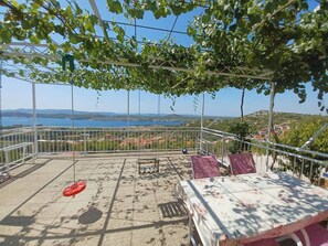 Una terraza con vistas al mar, una barandilla metálica y una mesa con mantel floreado.
