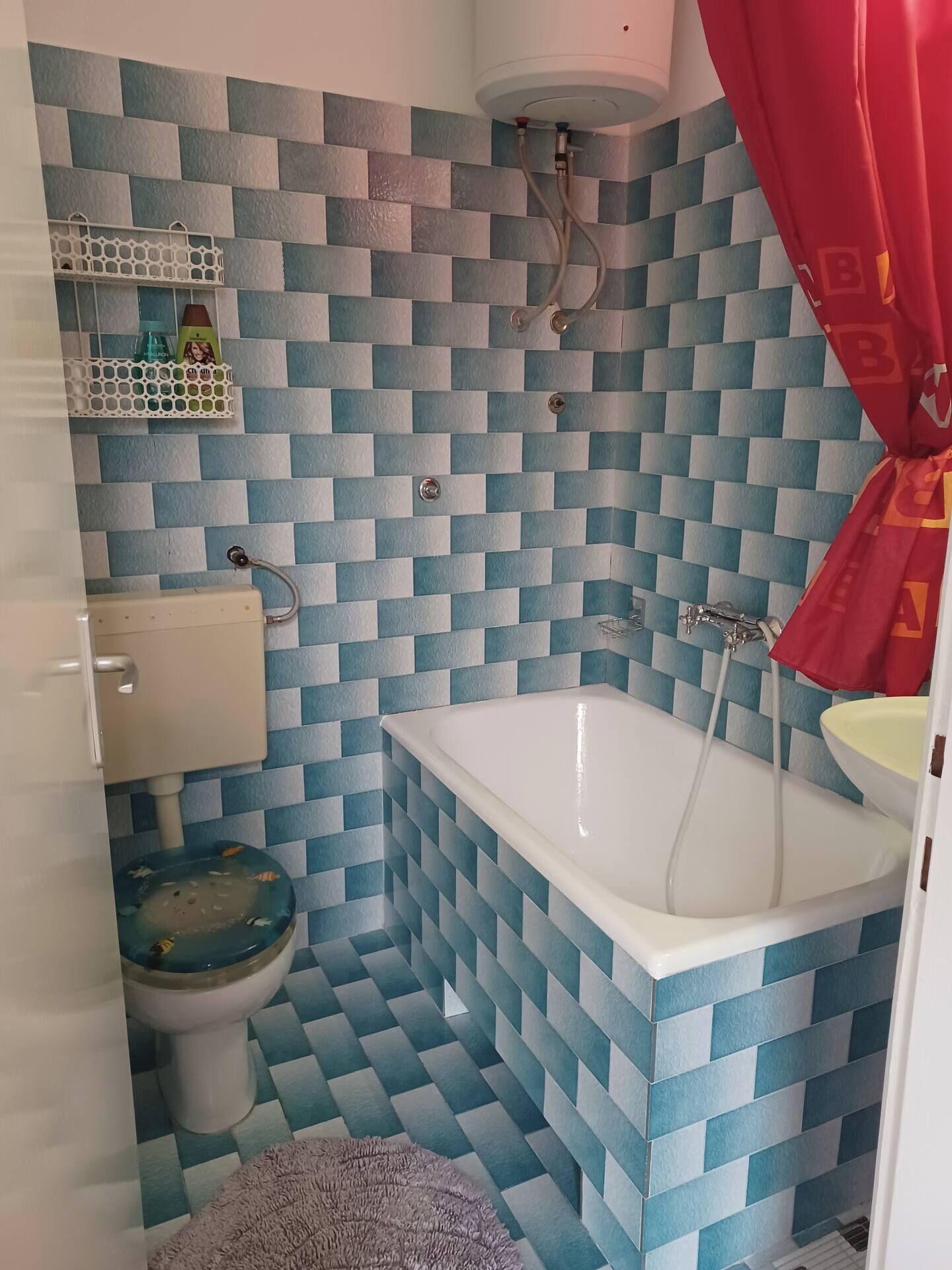 Un bagno con parete rivestita di piastrelle bianche e blu a scacchi, una vasca da bagno bianca, un water e una tenda da doccia rossa.