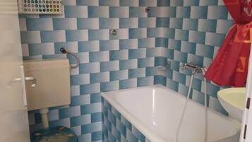 Un bagno con parete rivestita di piastrelle bianche e blu a scacchi, una vasca da bagno bianca, un water e una tenda da doccia rossa.