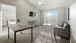 Una sala moderna con ventilador de techo, televisor montado en la pared, sofá, mesa de centro y mesa de comedor.