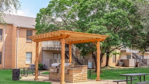 Un patio al aire libre con una pérgola de madera, una parrilla y mesas de picnic.