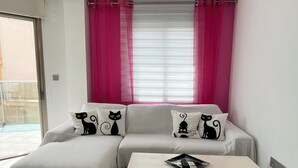 A modern living room with a sofa, two pillows with cat designs, a coffee table, and a window with pink curtains. - Sea sunrise (Guardamar del Segura)