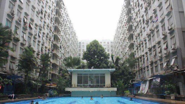 A swimming pool surrounded by high-rise residential buildings with balconies. - Daddy's Room Apartemen City Park (West Jakarta)