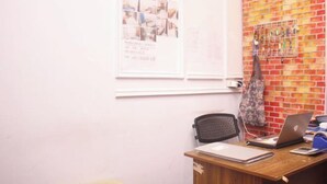 A small office with a wooden desk, a laptop, a chair, and a bulletin board with photos and notes. - Daddy's Room Apartemen City Park (West Jakarta)