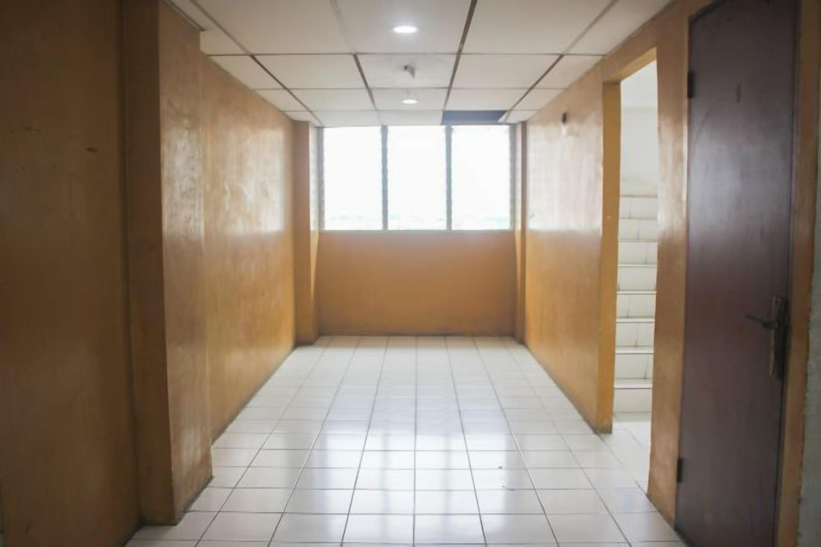 Un couloir carrelé, aux murs en bois, avec une porte au fond.