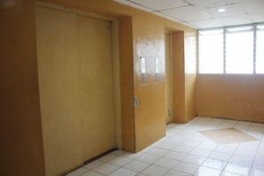 A hallway with a closed door, a window, and a tiled floor. - Daddy's Room Apartemen City Park (West Jakarta)