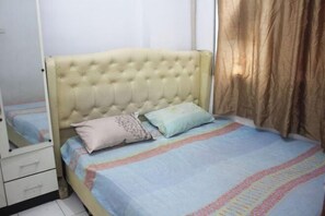 A bedroom with a tufted headboard, a bed with a patterned bedspread, a bedside table with drawers, and a mirror. - Daddy's Room Apartemen City Park (West Jakarta)