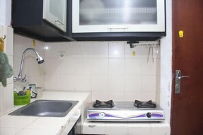 A compact kitchen with a sink, a stove, and a microwave. - Daddy's Room Apartemen City Park (West Jakarta)
