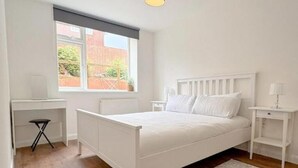 Ein Schlafzimmer mit einem weißen Bett, einem Schreibtisch und einem Fenster mit Blick auf eine Ziegelwand.