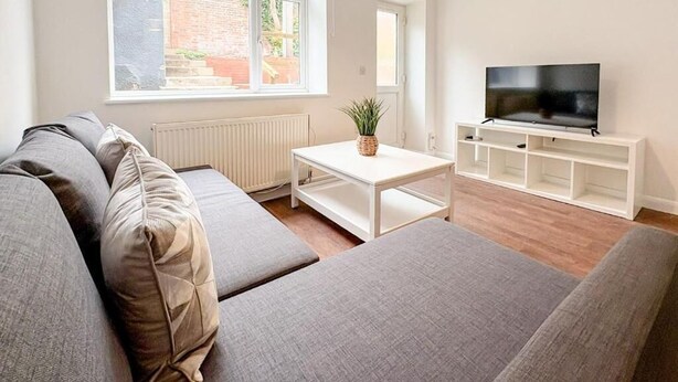 Ein modernes Wohnzimmer mit einer grauen Sofagarnitur, einem weißen Couchtisch und einem Flachbildfernseher auf einem weißen Schrank.