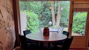 Ein runder Holztisch mit sechs Stühlen, einer Vase und Blick auf einen üppigen Garten durch eine Glastür.