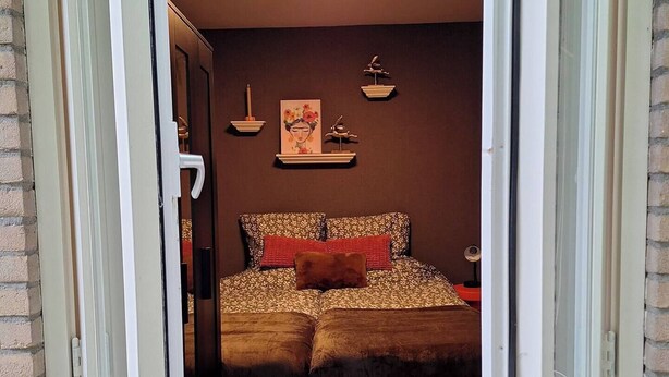 Ein offenes Fenster, das einen Schlafzimmer mit Bett, Kissen und Wanddekorationen zeigt.