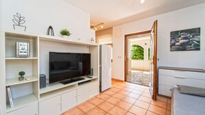 Ein modernes Wohnzimmer mit einem Flachbildfernseher, eingebauten Regalen, einer kleinen Pflanze und einer Tür, die auf einen Balkon führt.