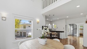 Une cuisine moderne avec des meubles blancs, un coin repas doté d’une table ronde en bois et un escalier menant à l’étage supérieur.