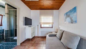 Un espacio habitable compacto con un televisor, un sofá, una ventana con persianas y un cuadro en la pared.