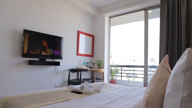Una camera d'albergo con un letto, una TV, una scrivania con una sedia, una finestra vista e una pianta in vaso.