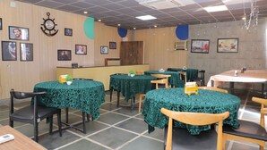 Un ristorante con tavoli rotondi ricoperti da tovaglie verdi, sedie in legno e quadri appesi alle pareti.