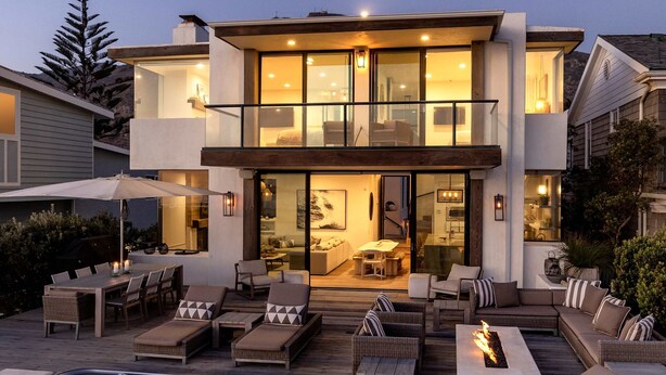 Une maison moderne à deux étages dotée d’un patio aménagé avec des meubles d’extérieur, un jacuzzi et une cheminée.