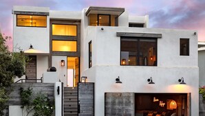 Un immeuble moderne à plusieurs étages, doté d’une entrée de garage, d’un espace extérieur aménagé pour s’asseoir et d’un escalier menant aux niveaux supérieurs.