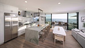 Une cuisine moderne dotée d’un grand îlot central, d’appareils électroménagers en acier inoxydable et offrant une vue sur l’océan.