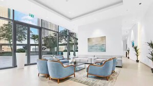 Un vestíbulo moderno con grandes ventanales, una zona de estar con sofás y sillones, y un diseño minimalista.