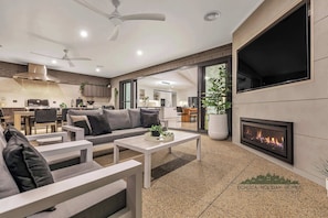A modern living room with a fireplace, a dining area, and a kitchen visible through a glass door. - 37 Sand Piper - Echuca Holiday Homes (Moama)