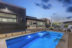 A modern pool area with a clear blue pool, a covered patio with outdoor seating, and a brick exterior wall. - 37 Sand Piper - Echuca Holiday Homes (Moama)