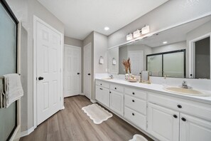 A bathroom with white cabinets, a large mirror, and a sink. - Downtown Oasis • Hot Tub + Game Room Fun - Cozy (Bentonville)
