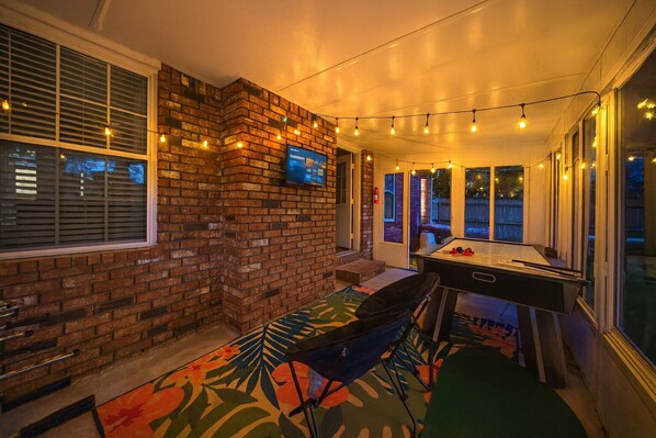 A cozy patio area with a brick wall, a pool table, and string lights. - Downtown Oasis • Hot Tub + Game Room Fun - Cozy (Bentonville)