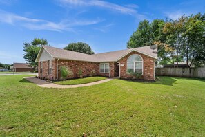 A single-story brick house with a front porch, a satellite dish, and a well-maintained lawn. - Downtown Oasis • Hot Tub + Game Room Fun - Cozy (Bentonville)