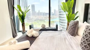 Ein Hotelzimmer mit einem großen Bett, zwei Zimmerpflanzen und Blick auf die Stadt sowie einem durch das Fenster sichtbaren Stadtpanorama.