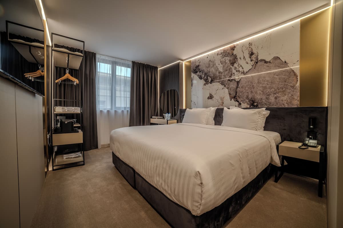 A modern hotel room with a large bed, bedside tables, a wardrobe, and a wall-mounted mirror.