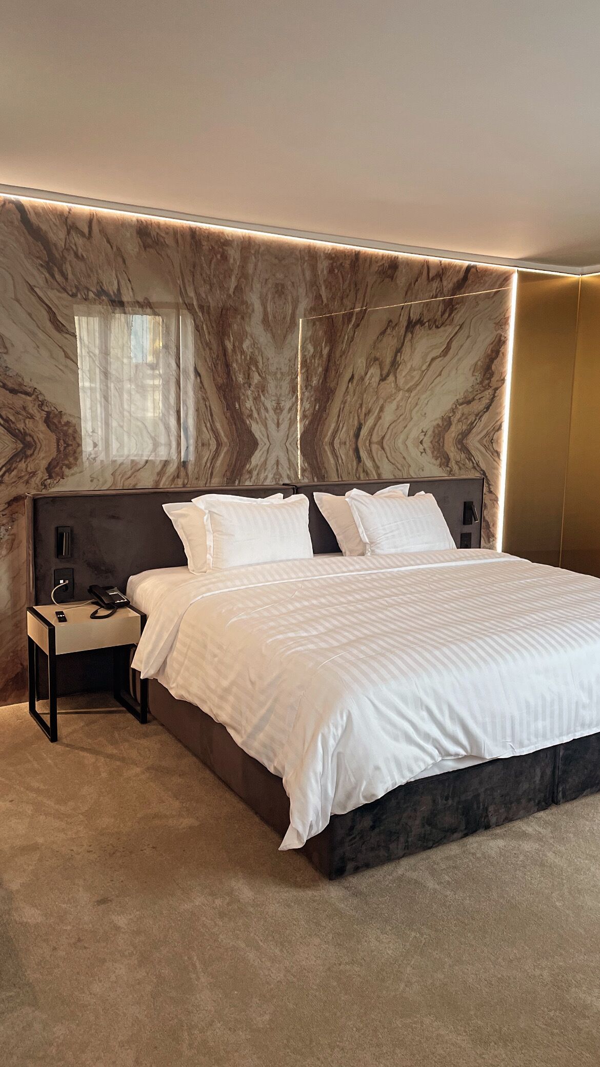 Un dormitorio moderno con una cama grande, una mesita de noche y una pared con diseño de mármol.