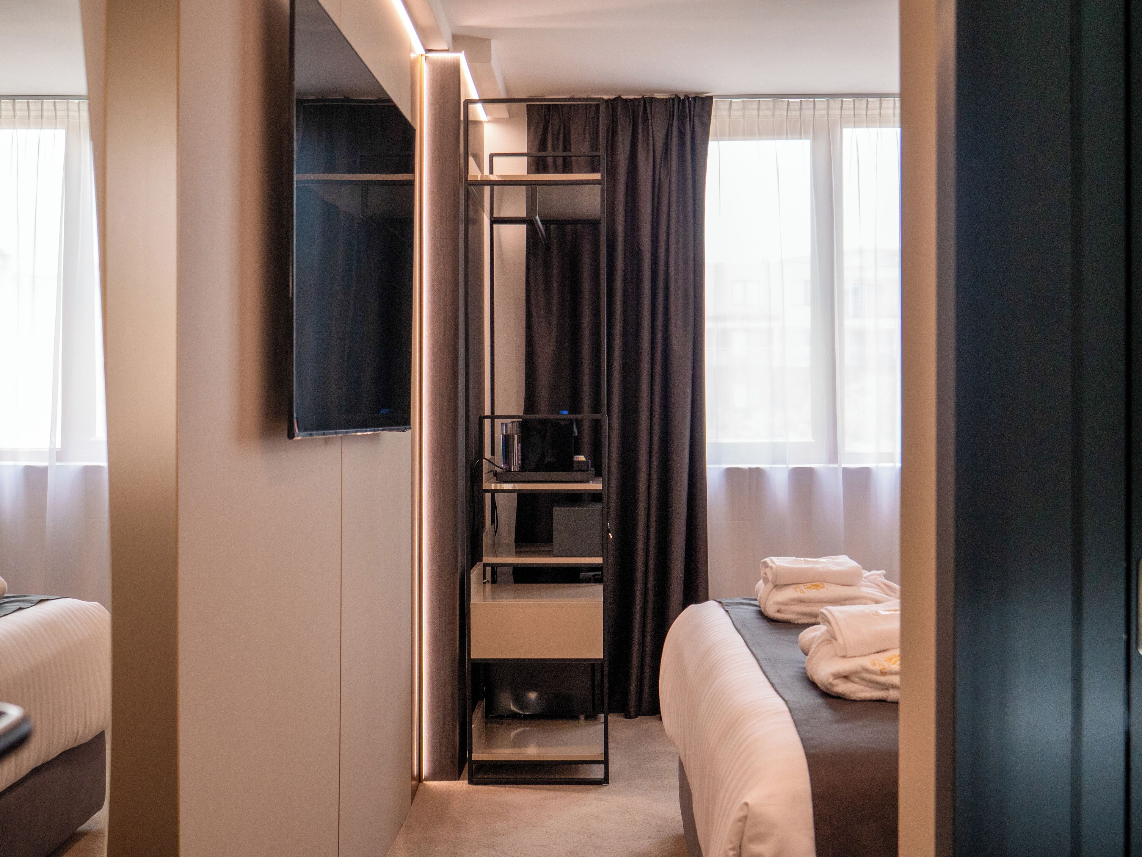 A hotel room with a bed, a TV mounted on the wall, a built-in shelf, and a window with curtains.